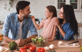 família preparando salada para o almoço, filha, alimentando o pai com uma fatia de pepino na cozinha