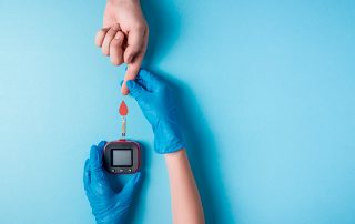 Enfermeiro de luvas azuis, segurando o dedo de uma paciente, com aparelho para medição de diabetes e ilustração de gota de sangue, sobre fundo azul.