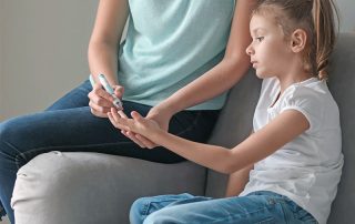 Mãe medindo a glicemia de filha pequena para medir a diabetes.