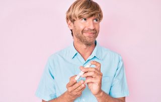 Homem branco, camisa azul de botão sobre fundo rosa, usando um medidor de glicemia, na dúvida se é possível deixar de ser diabético.