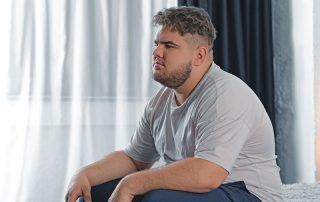 Homem com sobrepeso, sentado na cama pensativo, conceito de relação entra obesidade e testosterona.